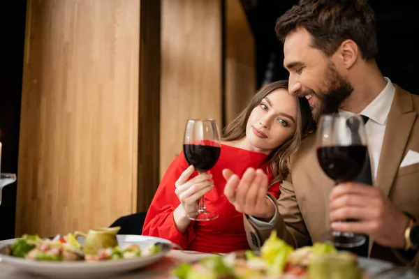 stock image young woman and cheerful man holding glasses with red wine during celebration on valentines day 