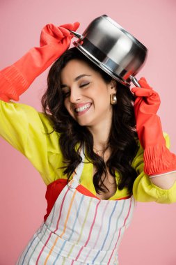 Kırmızı lastik eldivenli neşeli kadın pembe kafasında tencere tutarken eğleniyor.