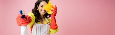 cheerful housewife in red rubber gloves obscuring face with rag and spraying from bottle isolated on pink, banner clipart