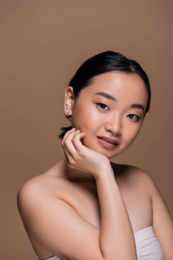 Portrait of smiling asian model looking at camera isolated on brown 