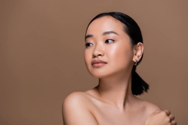 Young asian woman with naked shoulders looking away isolated on brown 