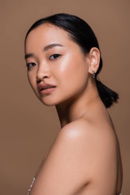 Pretty asian woman with makeup looking at camera isolated on brown 