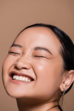 Portrait of pleased asian model closing eyes isolated on brown 