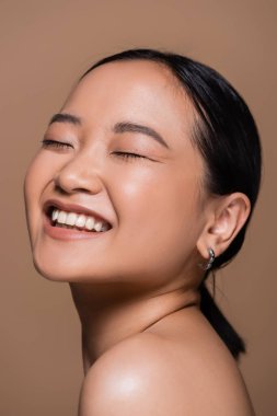 Pretty asian woman with closed eyes posing isolated on brown 