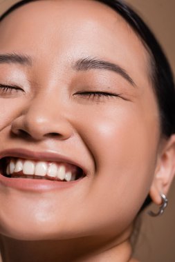 Cropped view of smiling asian woman closing eyes isolated on brown 