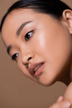 Close up view of asian woman with natural makeup looking away isolated on brown 