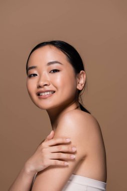 Brunette asian woman in top posing and looking at camera isolated on brown 