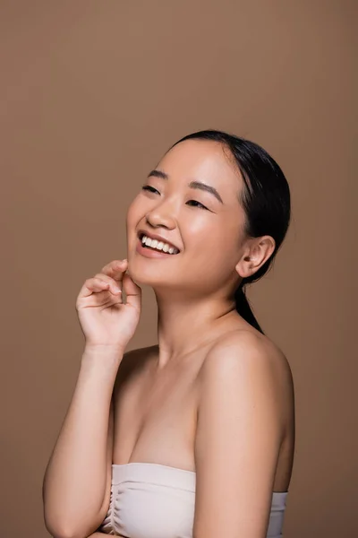 Positive Asian Woman Top Touching Face Looking Away Isolated Brown — Stock Photo, Image