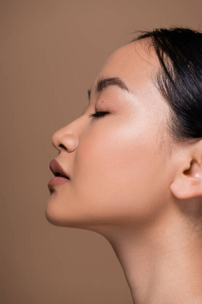 Side view of young asian woman with natural makeup isolated on brown 