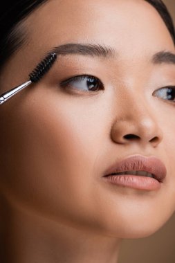 Cropped view of asian woman holding eyebrow brush isolated on brown 