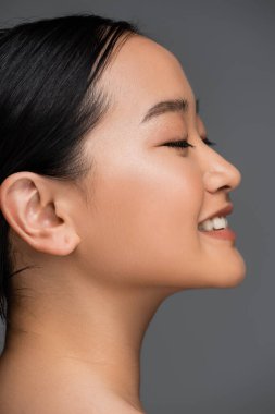 Side view of smiling asian woman closing eyes isolated on grey 