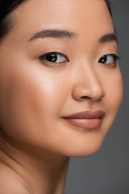 Close up view of young asian woman smiling and looking at camera isolated on grey 