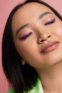 close up view of young asian woman with perfect makeup with blue eyeliner isolated on pink