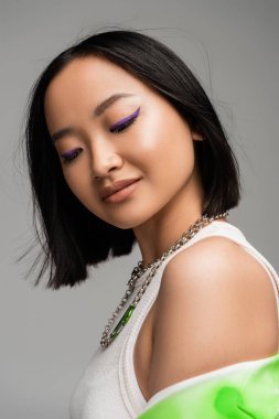 portrait of brunette asian woman with makeup and purple eyeliner isolated on grey