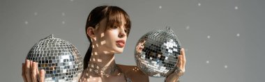 young woman holding shiny and vintage disco balls on grey background, banner 