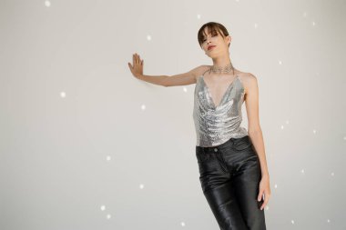 young woman in trendy top and leather pants leaning on grey wall 