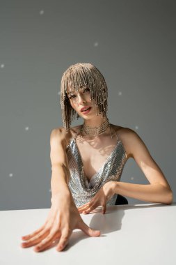 woman with metallic jewelry headwear posing while looking at camera on grey 