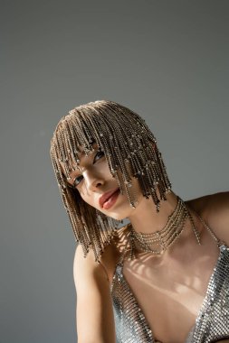 model with metallic headwear with jewelry looking at camera isolated on grey 