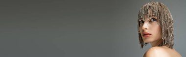 Young model with naked shoulder and jewelry headwear looking away isolated on grey, banner 