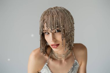 Fashionable woman in jewelry headwear looking at camera on grey background with light 