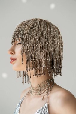 Side view of young woman in jewelry headwear posing on grey background with light 