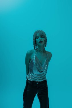 Fashionable model in top and jewelry headwear posing isolated on blue with lighting 