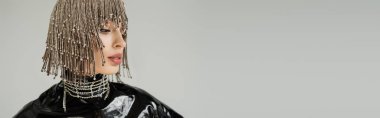 Pretty young model in jewelry headwear and latex clothes posing isolated on grey, banner