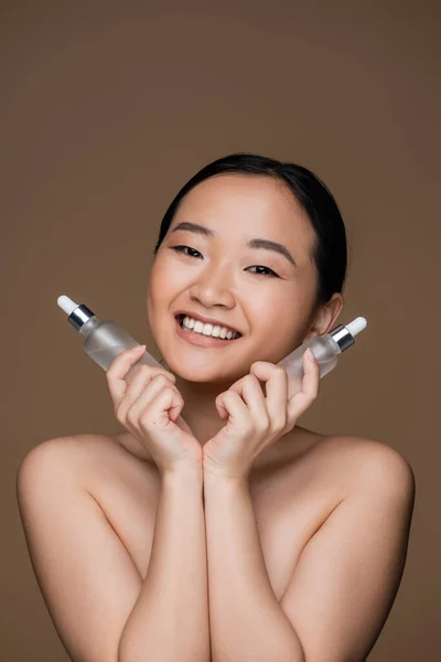 Cheerful Asian Woman Naked Shoulders Holding Cosmetic Serums Isolated Brown — Stock Photo, Image