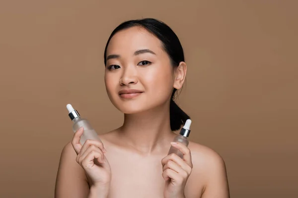 Pretty Asian Model Naked Shoulders Holding Cosmetic Serums Isolated Brown — Stock Photo, Image