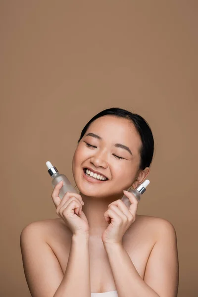 Pleased Asian Woman Holding Cosmetic Serums Isolated Brown — Stock Photo, Image