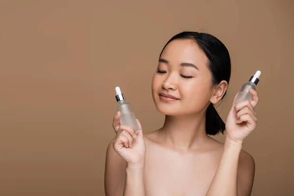 Pretty Asian Woman Naked Shoulders Holding Bottles Serums Isolated Brown — Stock Photo, Image