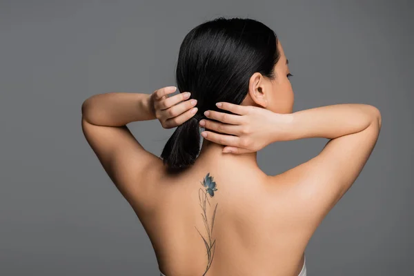 Brunette Asian Woman Tattoo Back Touching Ponytail Isolated Grey — Foto de Stock