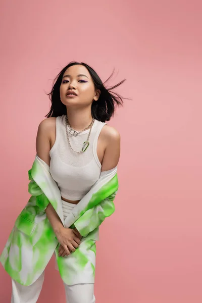 stock image brunette asian woman in white tank top and stylish jacket looking at camera isolated on pink