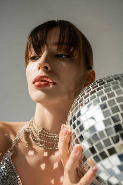 young woman with bangs holding shiny disco ball isolated on grey