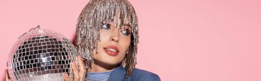 Stylish woman with makeup and jewelry headwear holding disco ball on pink background, banner 