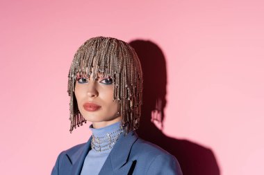 Fashionable woman in jewelry headwear looking at camera on pink background with shadow 
