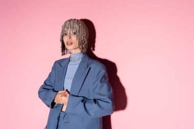Trendy young woman in jewelry headwear and blazer posing on pink background with shadow  