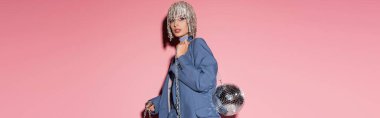 Stylish young woman in jewelry headwear and jacket holding disco ball on pink background, banner 