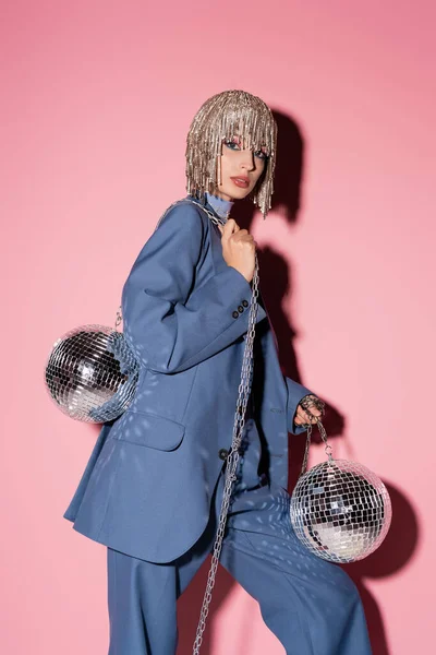 stock image Fashionable woman in luxury headwear holding disco balls on pink background with shadow 