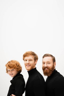 Siyah balıkçı yaka kazaklı kızıl saçlı ve sakallı neşeli adamlar gri renkli kameraya gülümsüyor.