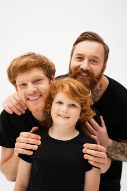 family portrait of redhead boy with happy father and bearded grandpa embracing isolated on grey clipart