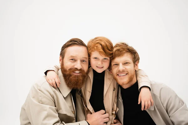 family portrait of redhead boy embracing happy redhead dad and bearded grandfather isolated on grey