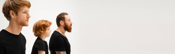 side view of bearded men and red haired kid in black t-shirts isolated on grey, banner