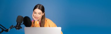 Teen girl looking at laptop near microphone isolated on blue, banner 