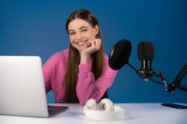 Teenager looking at camera near devices and microphone isolated on blue 