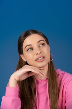 Portrait of teen girl in hoodie looking away isolated on blue 