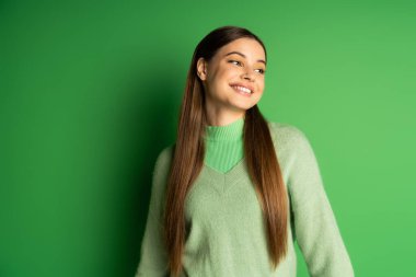 Smiling teenager in jumper looking away on green background 