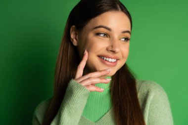 Portrait of smiling teenager in jumper posing on green background 