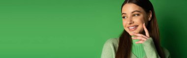 Positive teenage girl in jumper looking away on green background, banner 