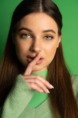 Portrait of teen girl showing secret gesture on green background 